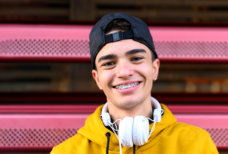 Teen wearing a backwards at and headphone smiling with braces